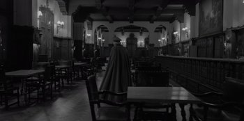 Movie still from “El Conde” (2023), directed by Pablo Larraín – A man in a black robe standing next to a table; Wide shot, High angle
