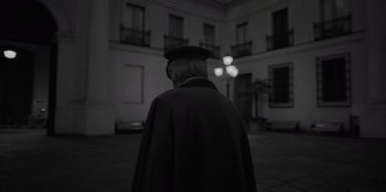 Movie still from “El Conde” (2023), directed by Pablo Larraín – A man wearing a black coat and a black hat; Medium shot, Low angle