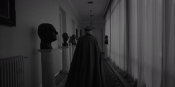 Movie still from “El Conde” (2023), directed by Pablo Larraín – A man wearing a cape walking down a hall way; Wide shot, Over the shoulder angle