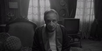 Movie still from “El Conde” (2023), directed by Pablo Larraín – An older man sitting in a chair in a living room; Medium shot, High angle
