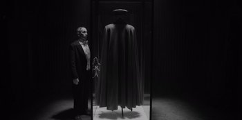 Movie still from “El Conde” (2023), directed by Pablo Larraín – A man standing next to a display case with a cape; Medium shot, Low angle