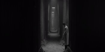 Movie still from “El Conde” (2023), directed by Pablo Larraín – A man in a trench coat standing in an alley way; Wide shot, High angle