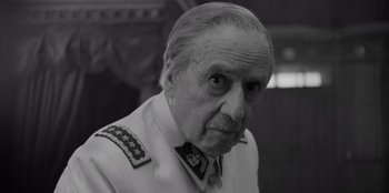 Movie still from “El Conde” (2023), directed by Pablo Larraín – An older man in a military uniform looking at the camera; Close Up shot, Over the shoulder angle