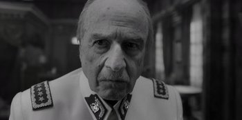 Movie still from “El Conde” (2023), directed by Pablo Larraín – An older man in a military uniform stares at the camera; Close Up shot, Low angle