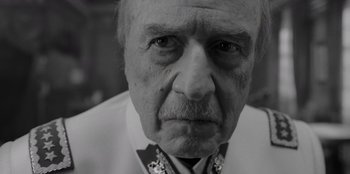 Movie still from “El Conde” (2023), directed by Pablo Larraín – An older man wearing a white shirt and a black tie; Close Up shot, Low angle