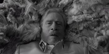 Movie still from “El Conde” (2023), directed by Pablo Larraín – An older man is laying in a pile of feathers; Close Up shot, Overhead angle
