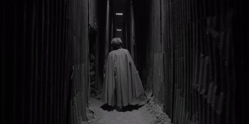 Movie still from “El Conde” (2023), directed by Pablo Larraín – A woman in a cape walking down a dark hallway; Wide shot, High angle
