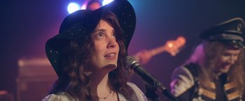 A woman wearing a black hat is singing into a microphone