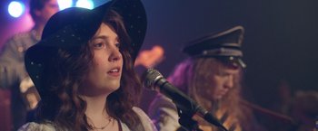 A woman in a cowboy hat sings into a microphone