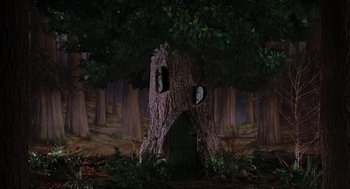 Movie still from “Elf” (2003), directed by Jon Favreau – A tree stump with a door and windows in the middle of the forest; Extreme Wide shot, Low angle