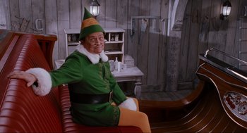 Movie still from “Elf” (2003), directed by Jon Favreau – A man dressed as buddy the elf sitting on a bench; Medium shot, Over the shoulder angle