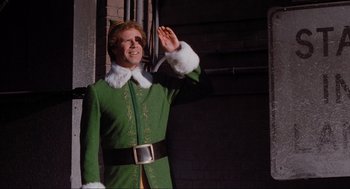 Movie still from “Elf” (2003), directed by Jon Favreau – A man dressed as buddy the elf waving; Medium shot, Low angle