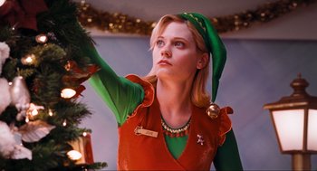 Movie still from “Elf” (2003), directed by Jon Favreau – A woman dressed as an elf holding up a christmas tree; Medium shot, Low angle