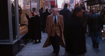 Movie still from “Elf” (2003), directed by Jon Favreau – A man in a long coat walking down the street; Medium shot, Over the shoulder angle