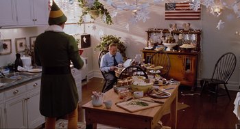 Movie still from “Elf” (2003), directed by Jon Favreau – A man sitting at a dining room table with an elf; Wide shot, High angle