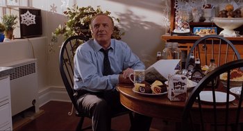 Movie still from “Elf” (2003), directed by Jon Favreau – An older man sitting at a table with a cup of coffee; Medium shot, Over the shoulder angle