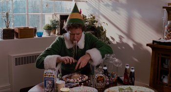 Movie still from “Elf” (2003), directed by Jon Favreau – A man dressed as a christmas elf eating a pizza; Medium shot, Overhead angle