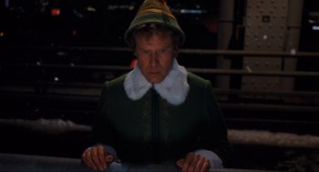 Movie still from “Elf” (2003), directed by Jon Favreau – A man dressed as buddy the elf is looking at the camera; Medium shot, Low angle