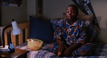 Movie still from “Elf” (2003), directed by Jon Favreau – A person sitting on a bed with a bowl of food; Medium shot, High angle