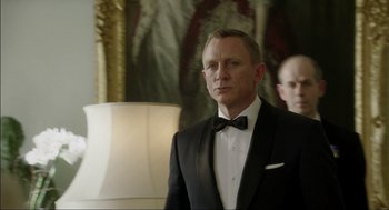 Movie still from “Elizabeth: A Portrait in Part(s)” (2022), directed by Roger Michell – A person wearing a suit and tie; Medium shot, Over the shoulder angle
