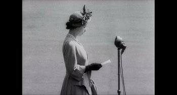 Movie still from “Elizabeth: A Portrait in Part(s)” (2022), directed by Roger Michell – An old photo of a woman standing in front of a microphone; Medium shot, Low angle