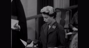 Movie still from “Elizabeth: A Portrait in Part(s)” (2022), directed by Roger Michell – An old black and white photo of a woman at a press conference; Close Up shot, Low angle