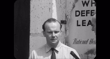Movie still from “Elizabeth: A Portrait in Part(s)” (2022), directed by Roger Michell – Black and white photograph of a man wearing a tie; Close Up shot, Low angle