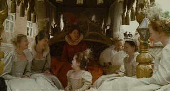 Movie still from “Elizabeth: A Portrait in Part(s)” (2022), directed by Roger Michell – A group of people sitting on top of a bed next to each other; Wide shot, High angle