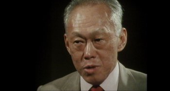 Movie still from “Elizabeth: A Portrait in Part(s)” (2022), directed by Roger Michell – An older asian man wearing a suit and tie; Close Up shot, Low angle