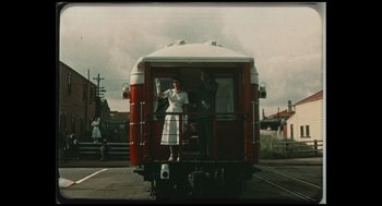 Movie still from “Elizabeth: A Portrait in Part(s)” (2022), directed by Roger Michell – Two people standing on the back of a train car; Extreme Wide shot, Low angle
