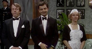 Movie still from “Elizabeth: A Portrait in Part(s)” (2022), directed by Roger Michell – A man in a tuxedo standing next to two other people; Medium shot, Over the shoulder angle