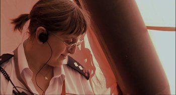 Movie still from “Elizabeth: A Portrait in Part(s)” (2022), directed by Roger Michell – A woman wearing glasses and a white shirt is listening to music; Close Up shot, Low angle