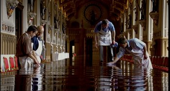 Movie still from “Elizabeth: A Portrait in Part(s)” (2022), directed by Roger Michell – Three people are cleaning the floor of a large room; Extreme Wide shot, High angle