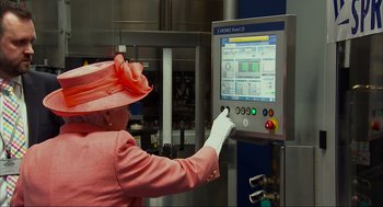 Movie still from “Elizabeth: A Portrait in Part(s)” (2022), directed by Roger Michell – An older woman in a pink dress and hat is using a machine; Close Up shot, Over the shoulder angle
