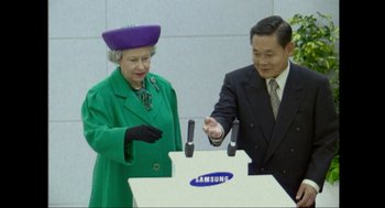 Movie still from “Elizabeth: A Portrait in Part(s)” (2022), directed by Roger Michell – A man and a woman standing in front of a samsung sign; Medium shot, Over the shoulder angle
