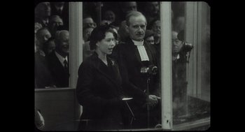 Movie still from “Elizabeth: A Portrait in Part(s)” (2022), directed by Roger Michell – An older man and woman standing next to each other in front of a crowd; Medium shot, Low angle