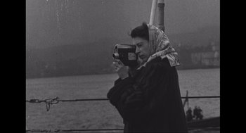 Movie still from “Elizabeth: A Portrait in Part(s)” (2022), directed by Roger Michell – An old black and white photo of a woman holding a video camera; Medium shot, Low angle