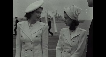 Movie still from “Elizabeth: A Portrait in Part(s)” (2022), directed by Roger Michell – A couple of women standing next to each other on a street; Medium shot, Low angle