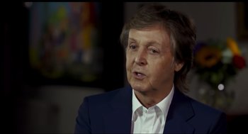 Movie still from “Elizabeth: A Portrait in Part(s)” (2022), directed by Roger Michell – A person wearing a suit and tie; Close Up shot, Over the shoulder angle