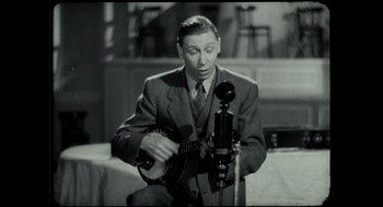 Movie still from “Elizabeth: A Portrait in Part(s)” (2022), directed by Roger Michell – A black and white photo of a man playing a guitar; Medium shot, High angle