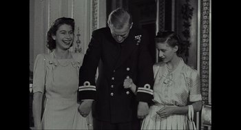 Movie still from “Elizabeth: A Portrait in Part(s)” (2022), directed by Roger Michell – Two women and a man in a dress uniform holding hands; Medium shot, Low angle