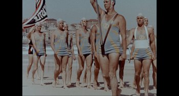 Movie still from “Elizabeth: A Portrait in Part(s)” (2022), directed by Roger Michell – A group of men standing on top of a sandy beach; Wide shot, Low angle