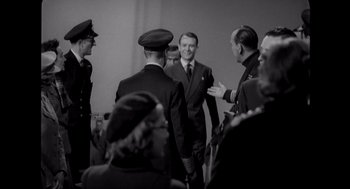 Movie still from “Elizabeth: A Portrait in Part(s)” (2022), directed by Roger Michell – A group of men standing next to each other in a room; Medium shot, Over the shoulder angle
