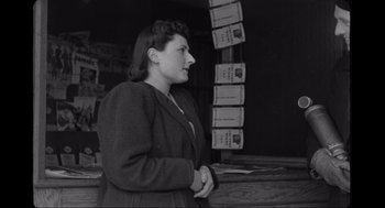 Movie still from “Elizabeth: A Portrait in Part(s)” (2022), directed by Roger Michell – An old black and white photo of a woman standing in front of a bunch of papers; Medium shot, Low angle