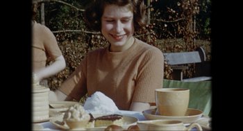 Movie still from “Elizabeth: A Portrait in Part(s)” (2022), directed by Roger Michell – A woman sitting at a table with a plate of food; Medium shot, High angle