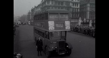 Movie still from “Elizabeth: A Portrait in Part(s)” (2022), directed by Roger Michell – An old double decker bus driving down a street; Extreme Wide shot, Low angle