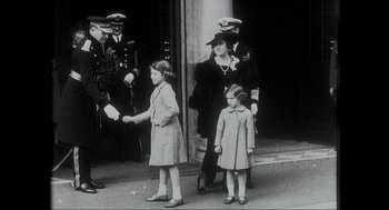 Movie still from “Elizabeth: A Portrait in Part(s)” (2022), directed by Roger Michell – A group of people standing next to each other on a street; Wide shot, Over the shoulder angle