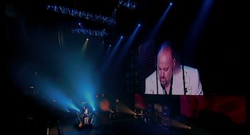 Movie still from “Elizabeth: A Portrait in Part(s)” (2022), directed by Roger Michell – A man is sitting in front of a large screen; Extreme Wide shot, High angle