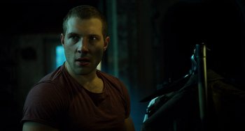 Movie still from “A Good Day to Die Hard” (2013), directed by John Moore – A man in a red t - shirt is standing next to another man; Close Up shot, Over the shoulder angle