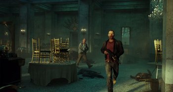 Movie still from “A Good Day to Die Hard” (2013), directed by John Moore – A man holding a gun while standing next to a table; Wide shot, High angle